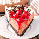 Slice of black forest cheesecake on white round plate.