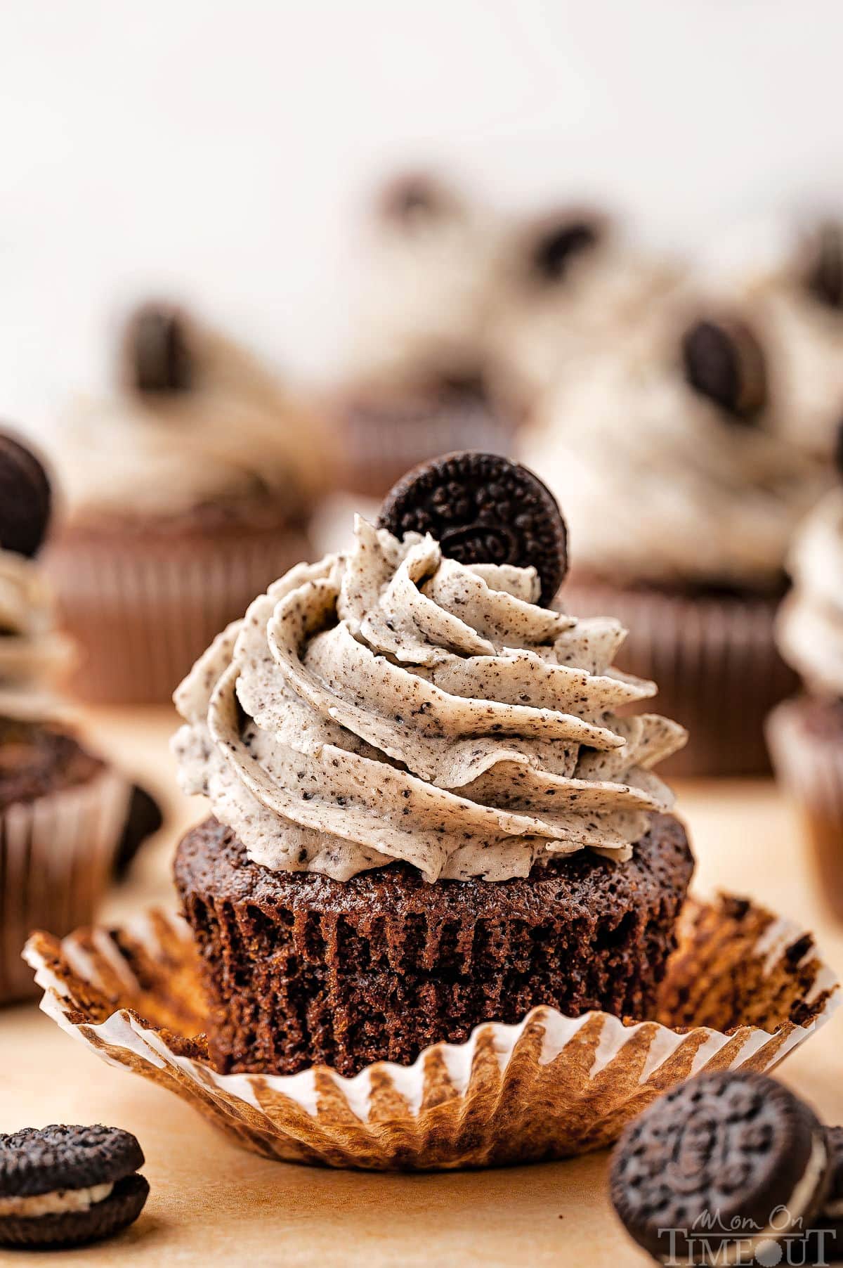 Close up of an Oreo Cupcake with extra cupcakes in the background. Mini Oreos are sitting by the cupcake.