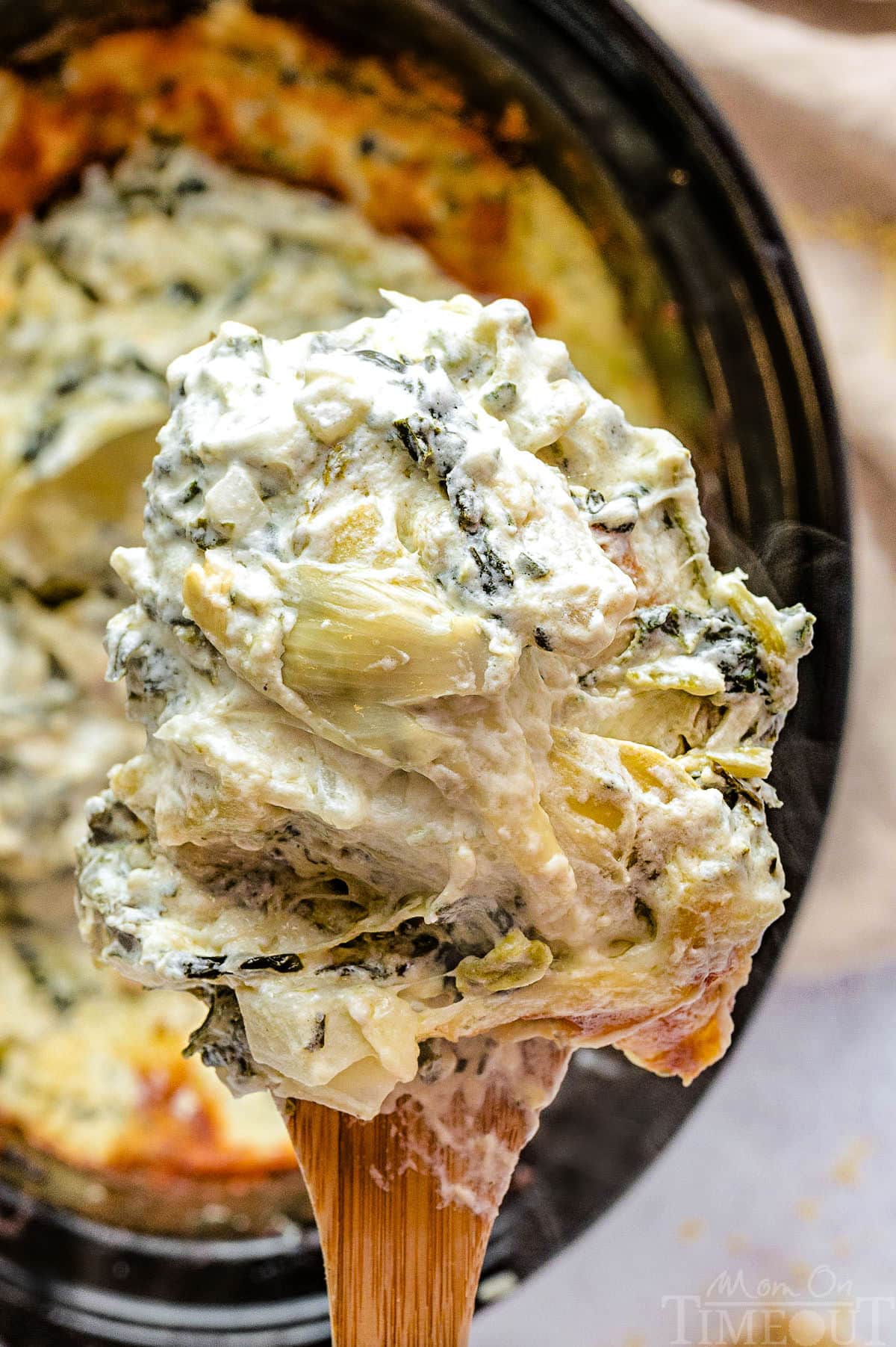 Crockpot spinach and artichoke dip scooped up with a large wooden spoon.