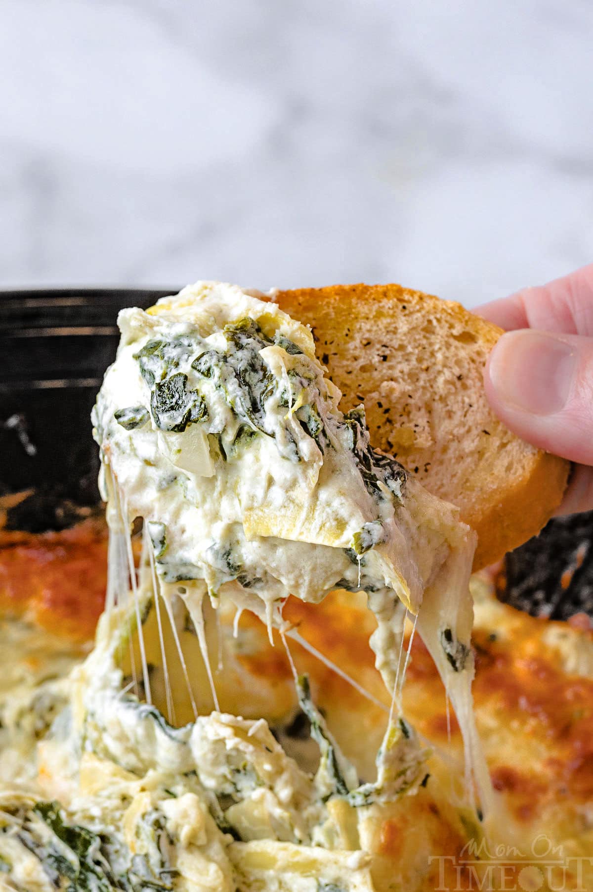 Crostini dipping into crockpot spinach artichoke dip recipe.