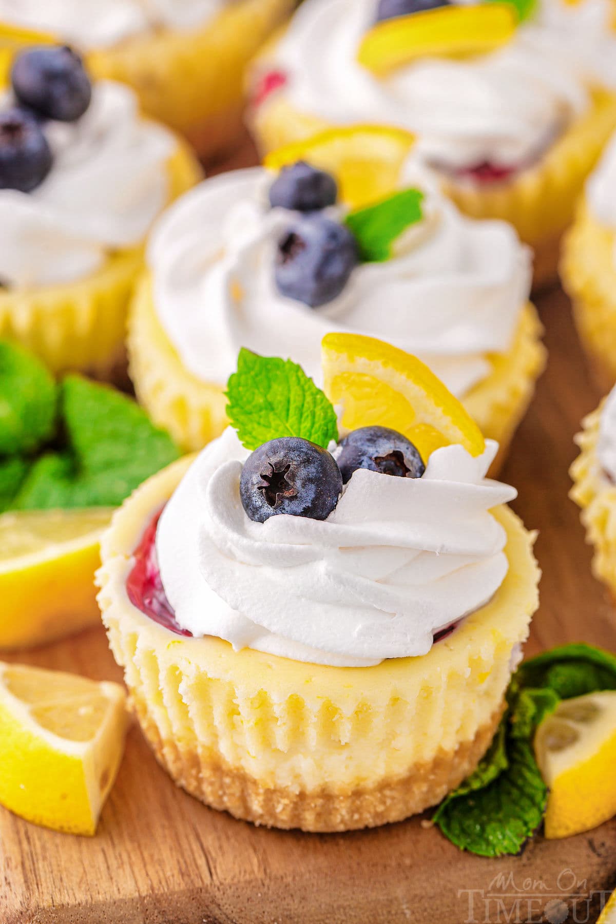 A close up view of a lemon blueberry mini cheesecake. Garnishes and more cheesecakes are behind it.