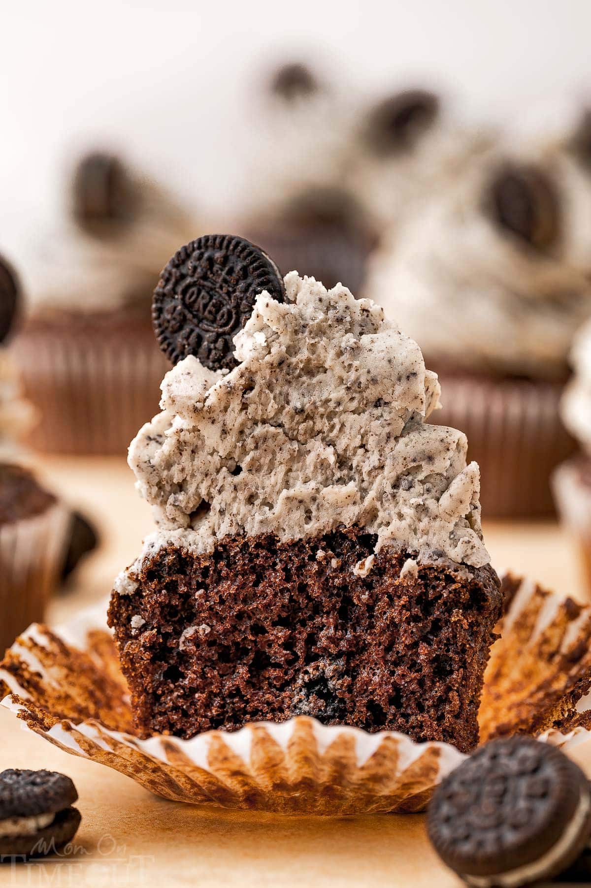 An oreo cupcake cut in half to show the detail of the cake and frosting close up. More cupcakes are in the background.