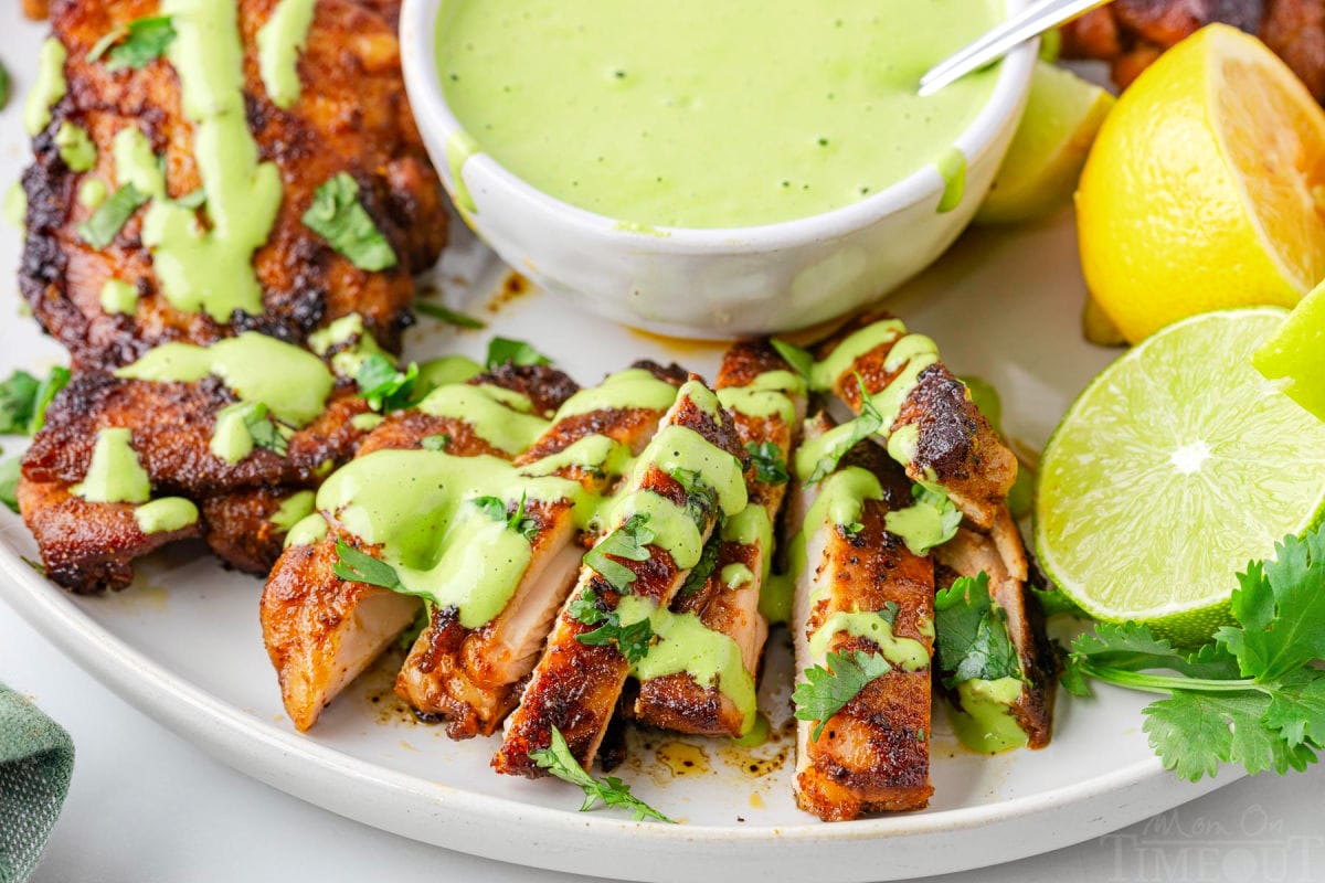 Aji verde sauce drizzled over Peruvian chicken on white plate next to limes.