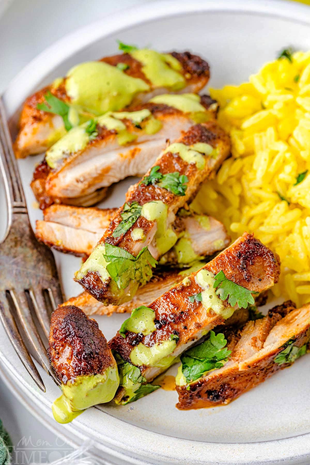 Sliced Peruvian Chicken next to a side of rice on a white plate with a fork holding a piece.