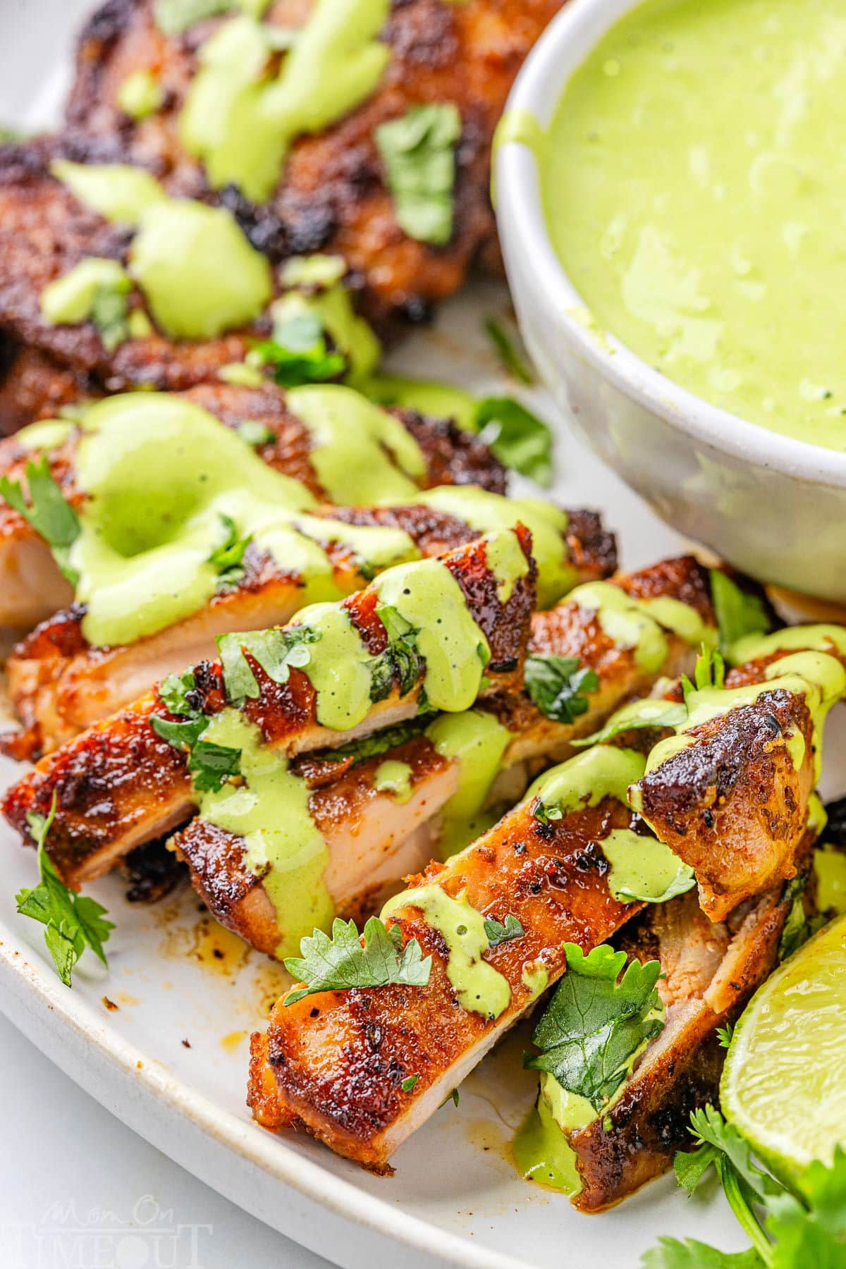 Close up view of slices of Peruvian Chicken drilled with Aji Verde on a white serving plate.