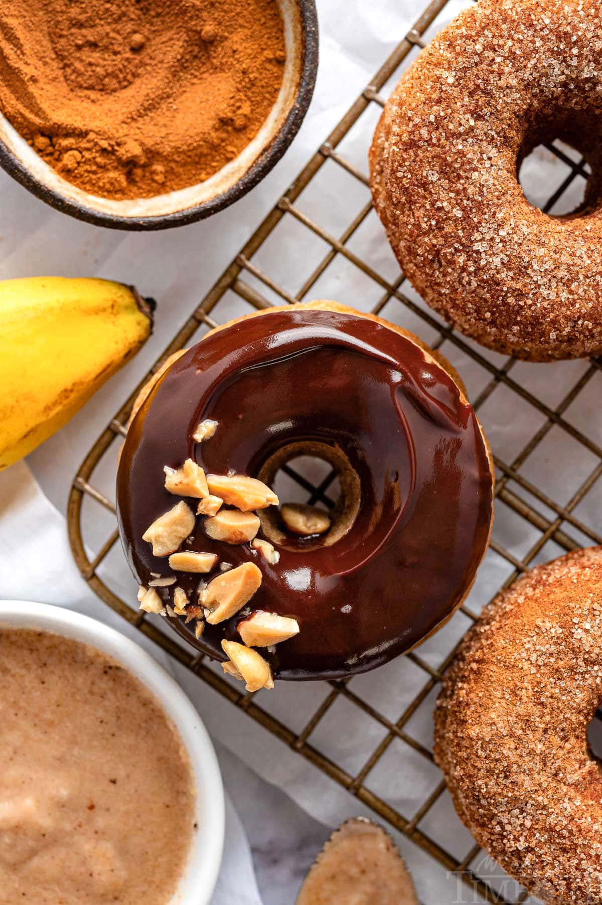 Chocolate glazed banana donut on cooling rack to cinnamon sugar banana donuts.