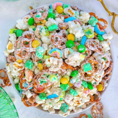 Top down view of Leprechaun Bait snack mix in white round bowl. Brass tongs are sitting next to the bowl.