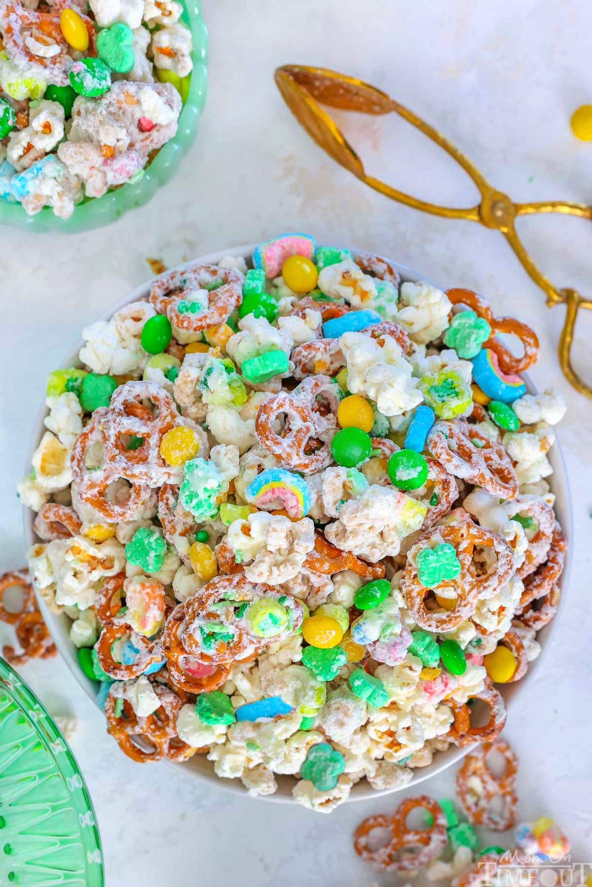 Top down view of Leprechaun Bait snack mix in white round bowl. Brass tongs are sitting next to the bowl.