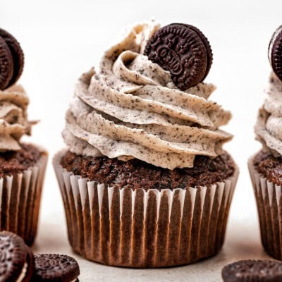 Three cookies and cream cupcakes lined up and topped with oreo frosting and a mini oreo on a white background.